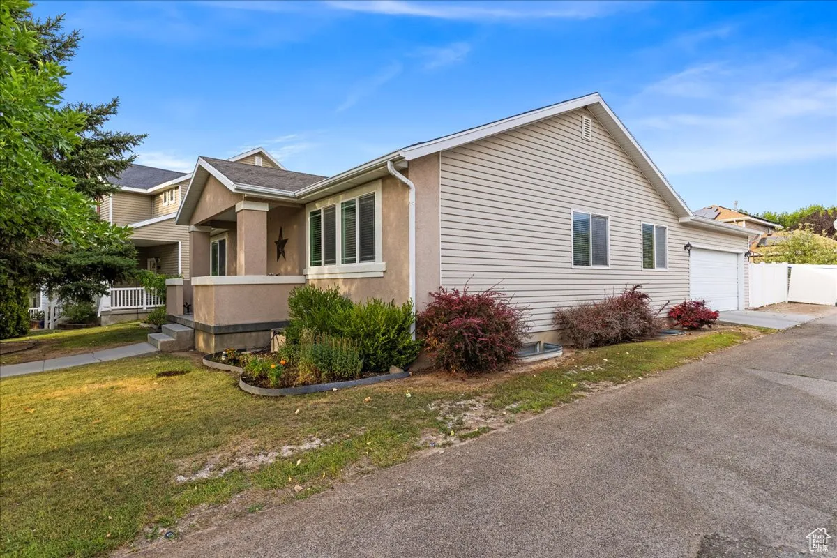 View of side of home with an attached garage, a porch, a lawn, asphalt driveway, and stucco siding