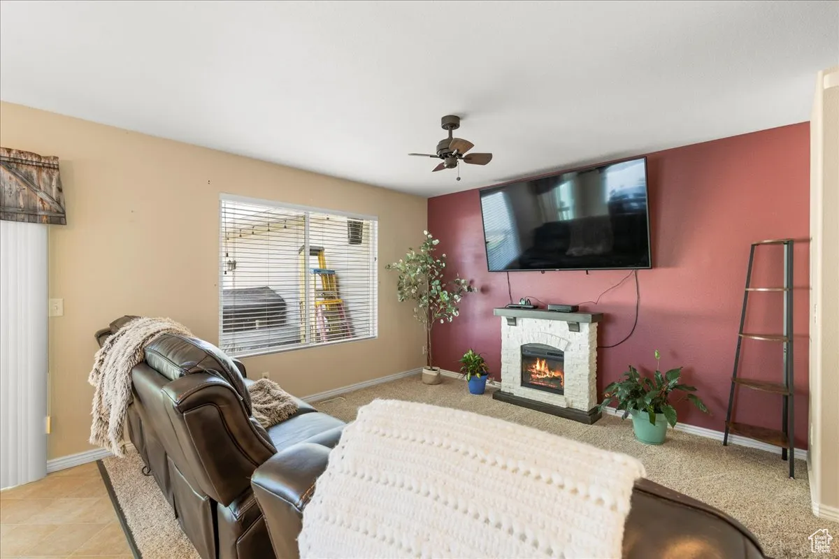 Carpeted living room with a stone fireplace and ceiling fan