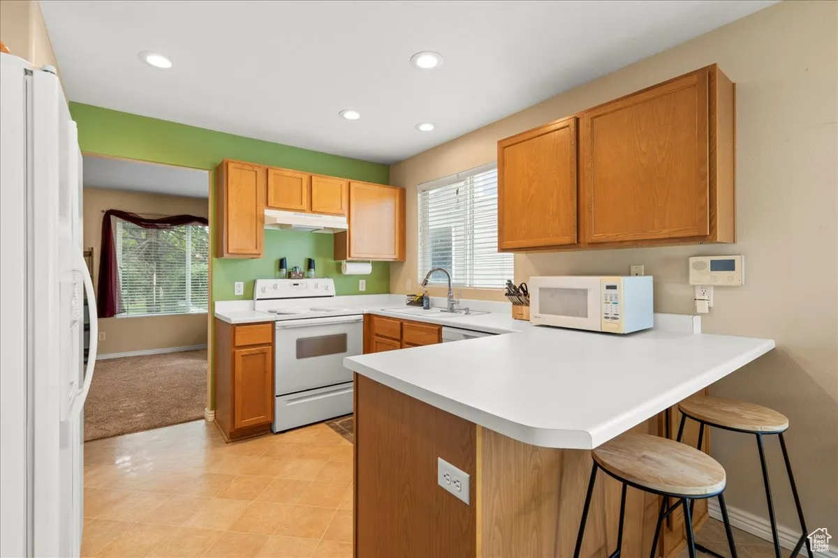 Kitchen featuring a breakfast bar area, white appliances, a peninsula, light countertops, and recessed lighting