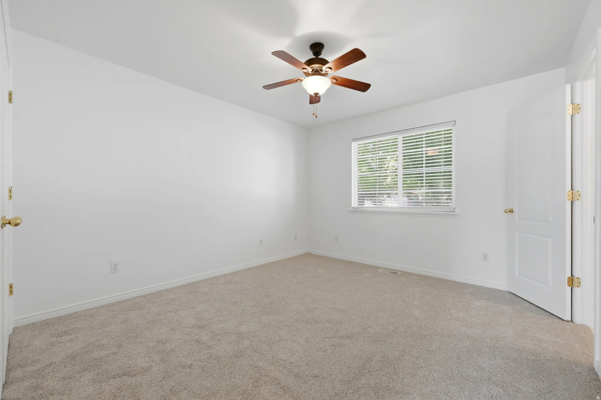 Carpeted room featuring a window with horizontal blinds, a ceiling fan with integrated lighting, and a white paneled door with brass hardware