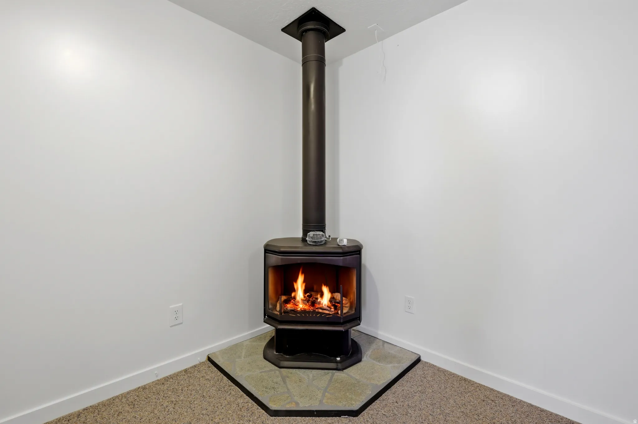 Freestanding wood-burning stove with a glass front, set on a corner tile hearth