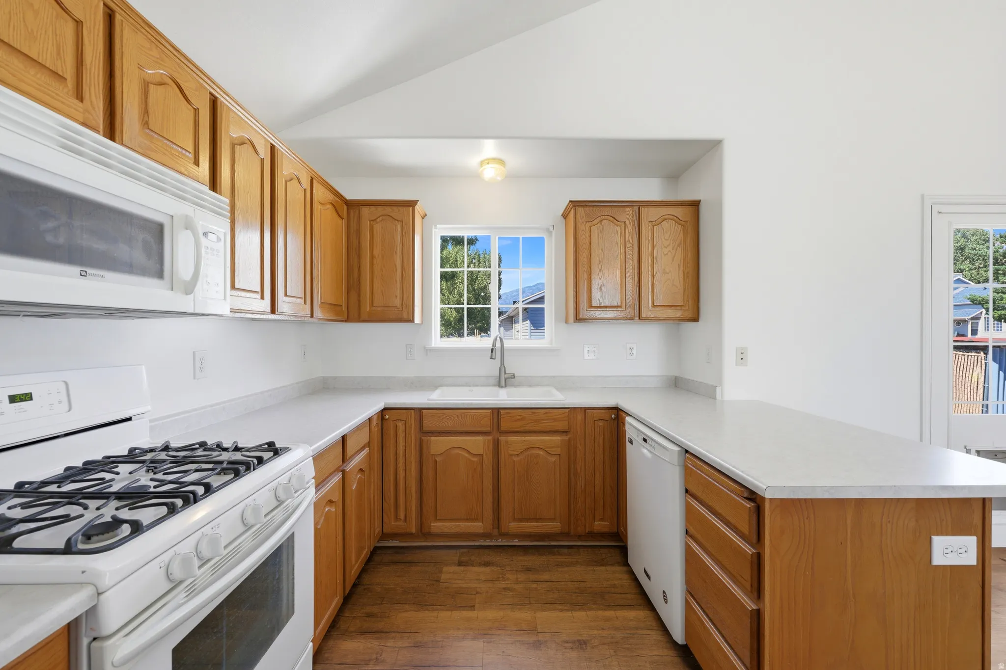 Kitchen featuring wood-finish cabinetry, solid surface countertops, a white gas range with overhead microwave, and a double basin sink beneath a window