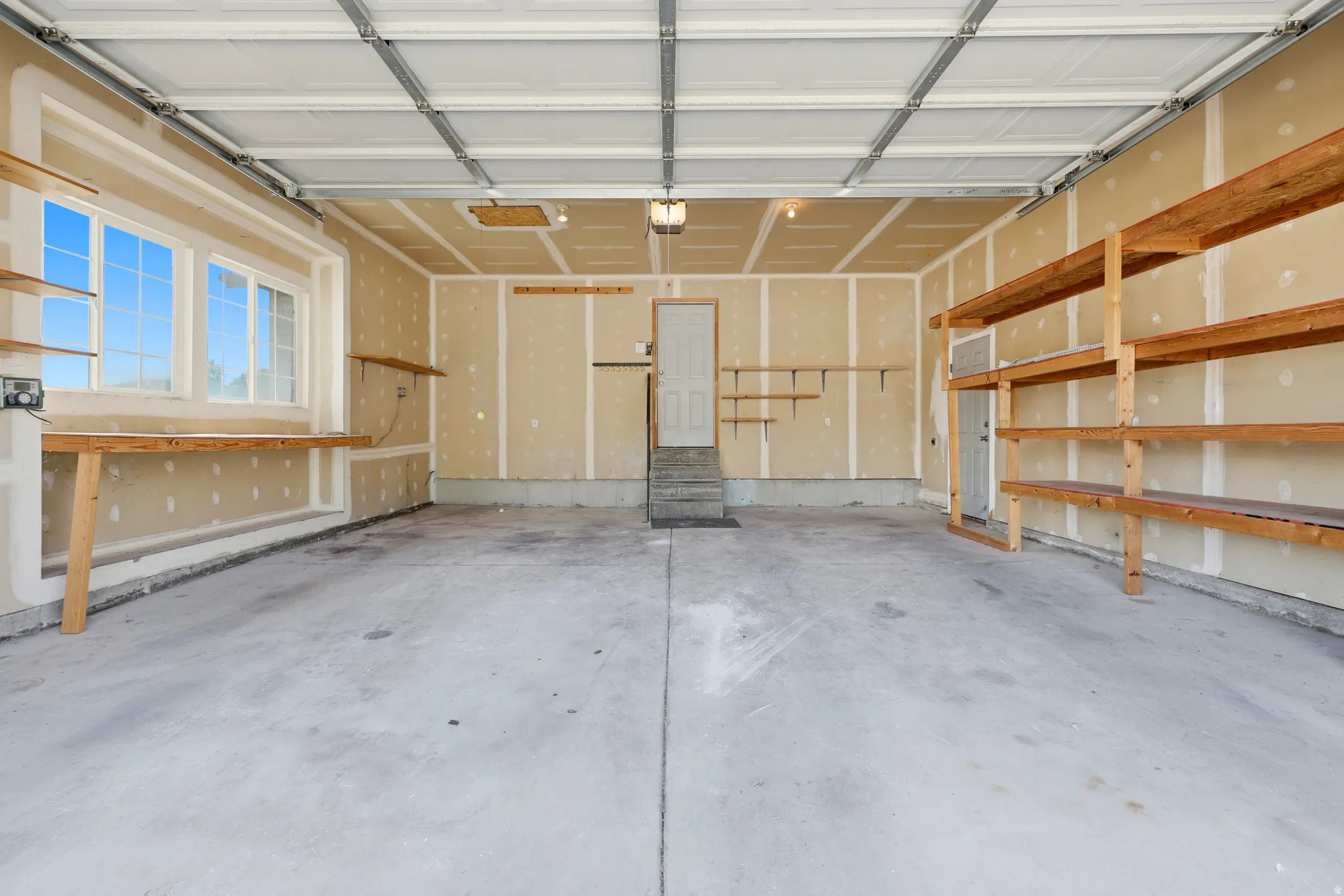 Spacious garage featuring a concrete floor, built-in shelving, a workbench, and multiple windows providing natural light