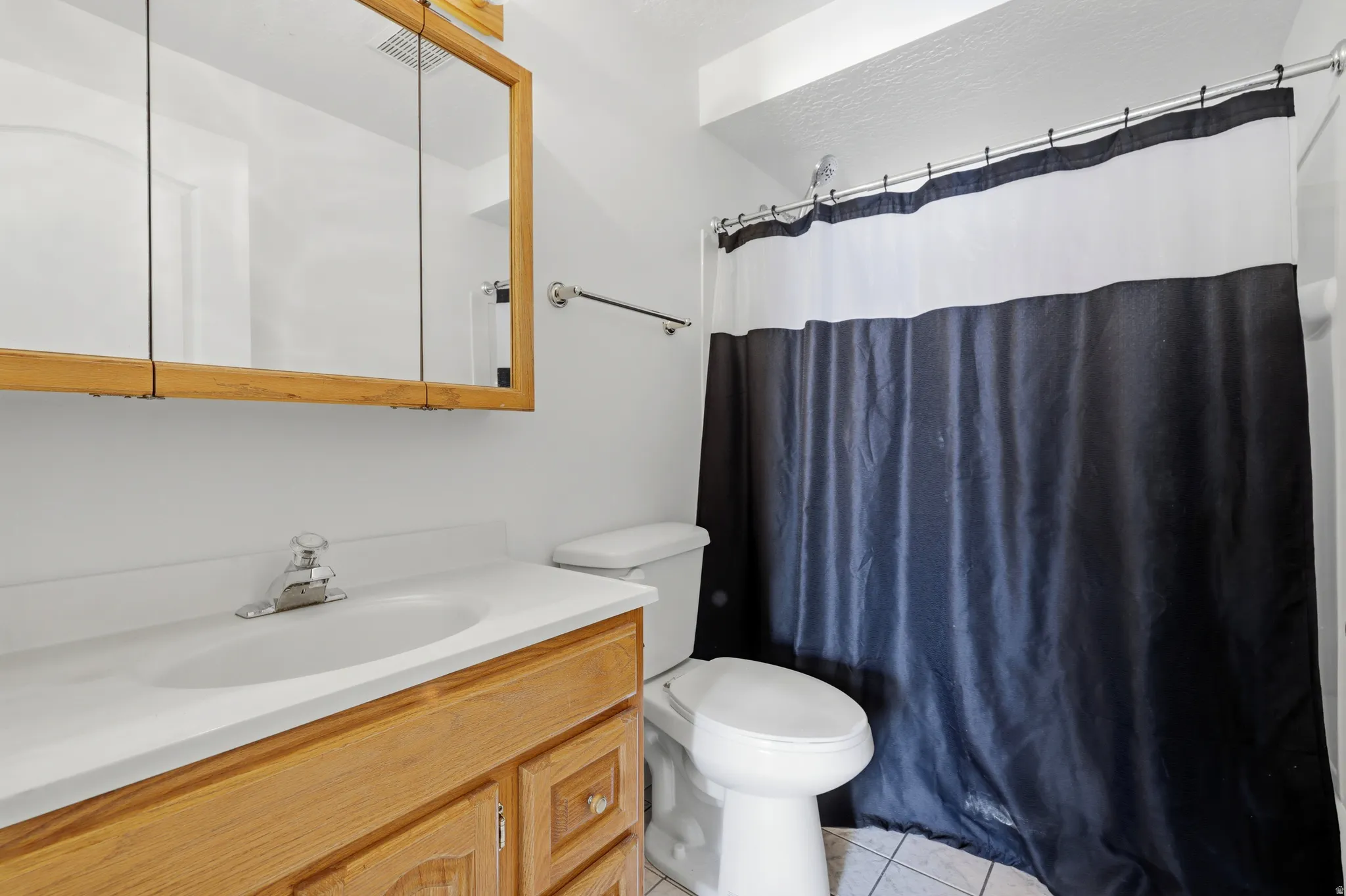 Bathroom featuring a wood-finish vanity with a white countertop and integrated sink, a matching wood-finish medicine cabinet, a toilet, and tile flooring