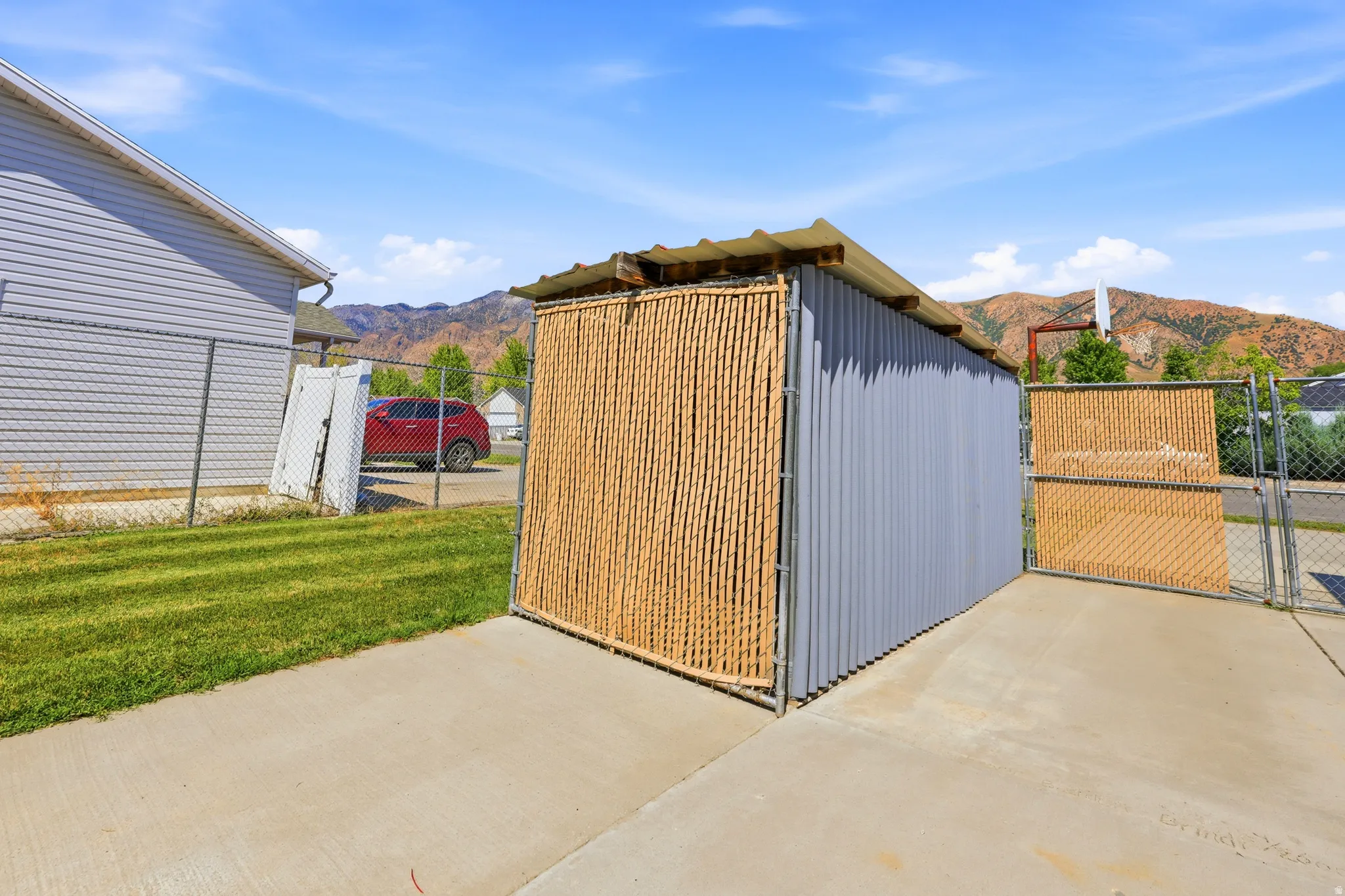 Outdoor storage structure with corrugated metal siding and bamboo screening, featuring a chain-link fence and concrete pad