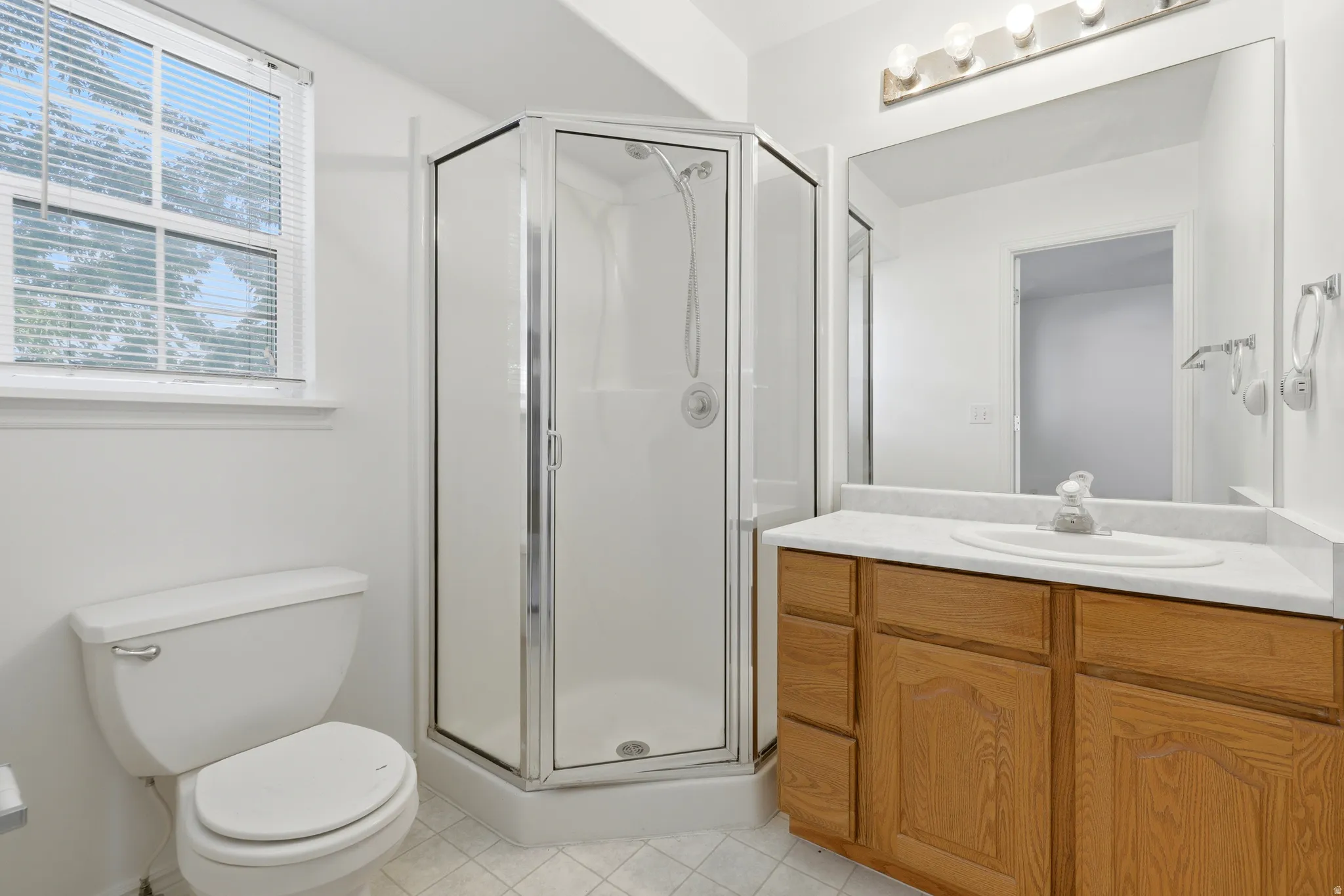 Bathroom featuring a corner shower enclosure, window with blinds, and white toilet
