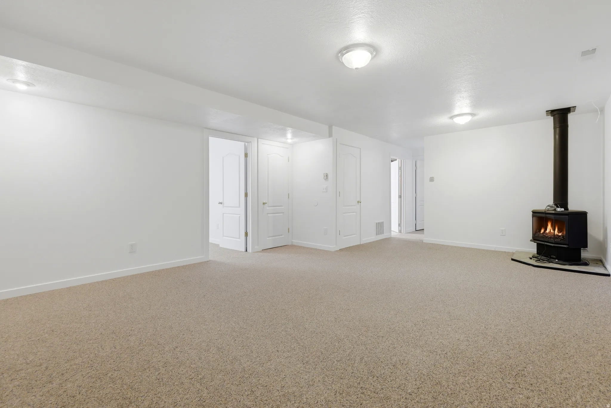 Expansive room with neutral carpeting, a freestanding fireplace, white walls, and multiple white paneled doors