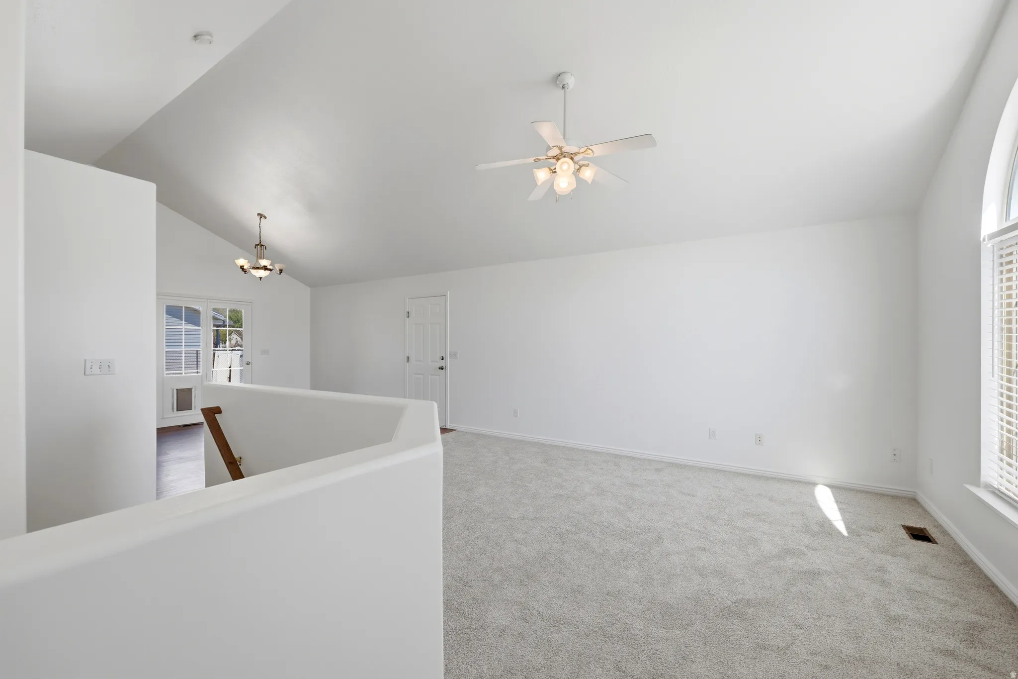 Spacious living area featuring vaulted ceilings, light-hued carpet flooring, and an arched window with louvered blinds