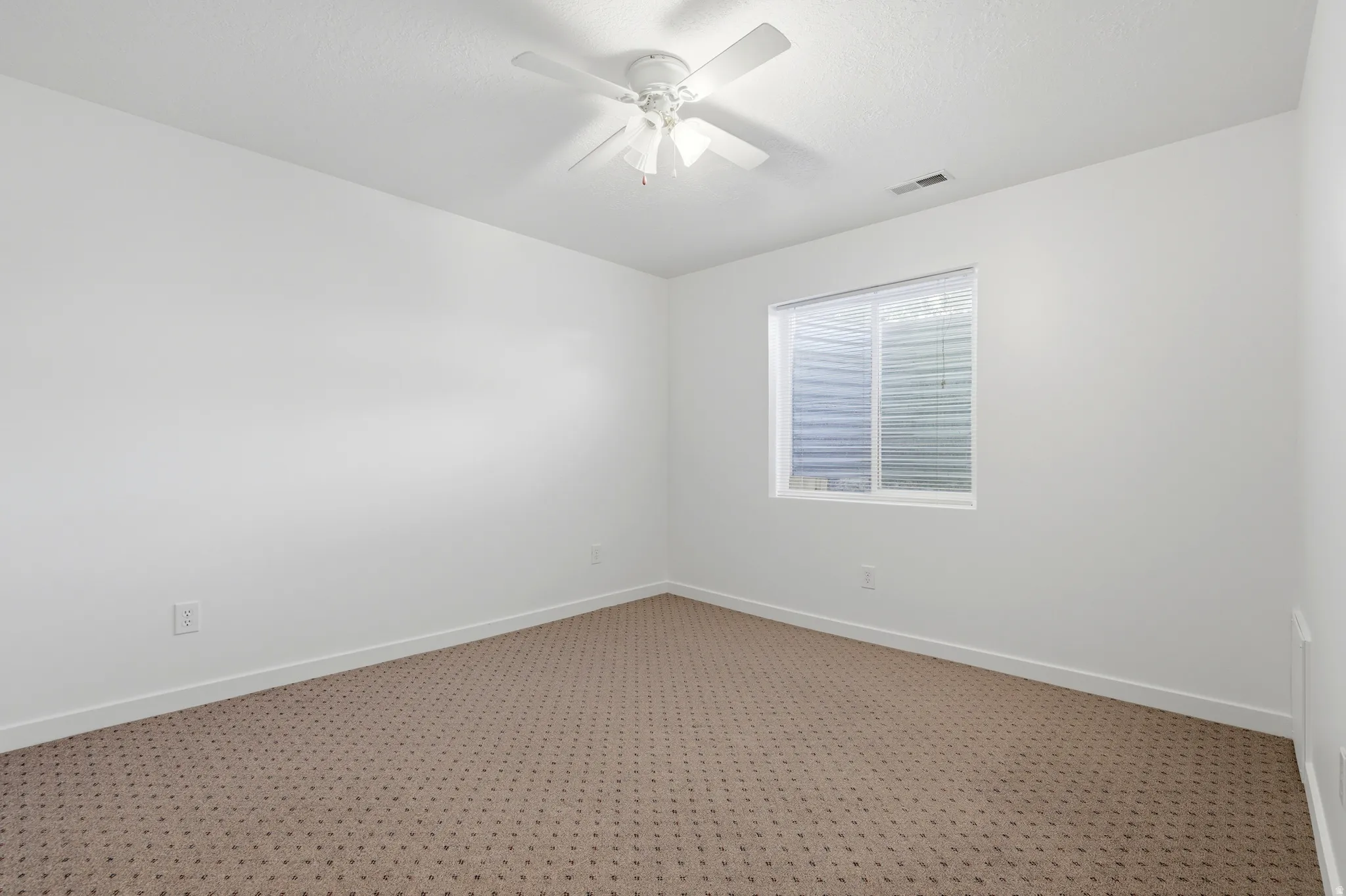 Room featuring patterned carpet flooring, white walls, and a white ceiling fan with integrated lighting