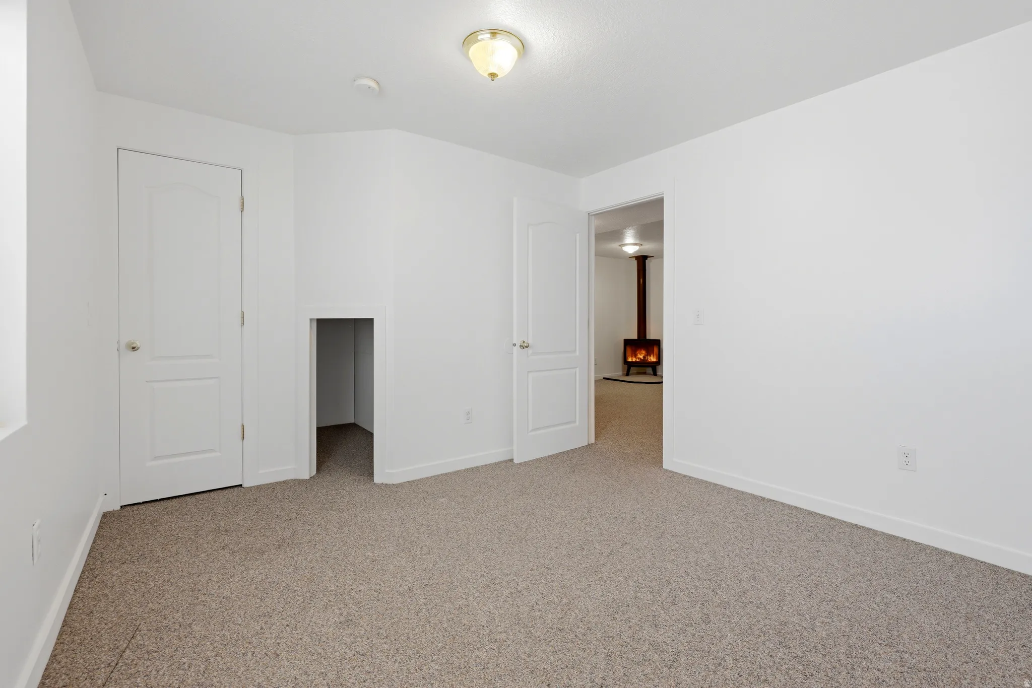 Carpeted room with white walls, a flush-mount ceiling light fixture, a closed white panel door, and an open doorway leading to another area