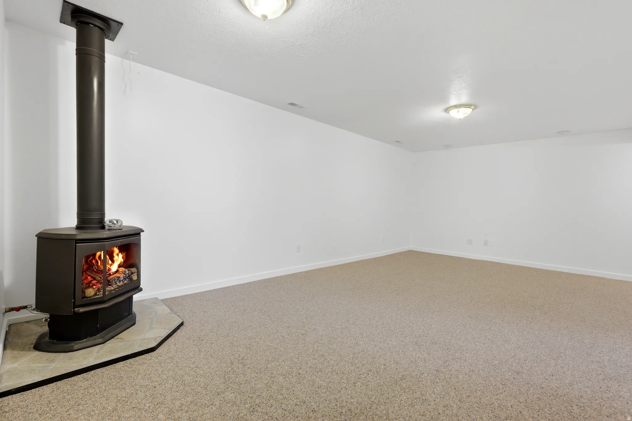 Freestanding wood-burning stove with a corner tile hearth, carpeted flooring, and recessed ceiling lighting