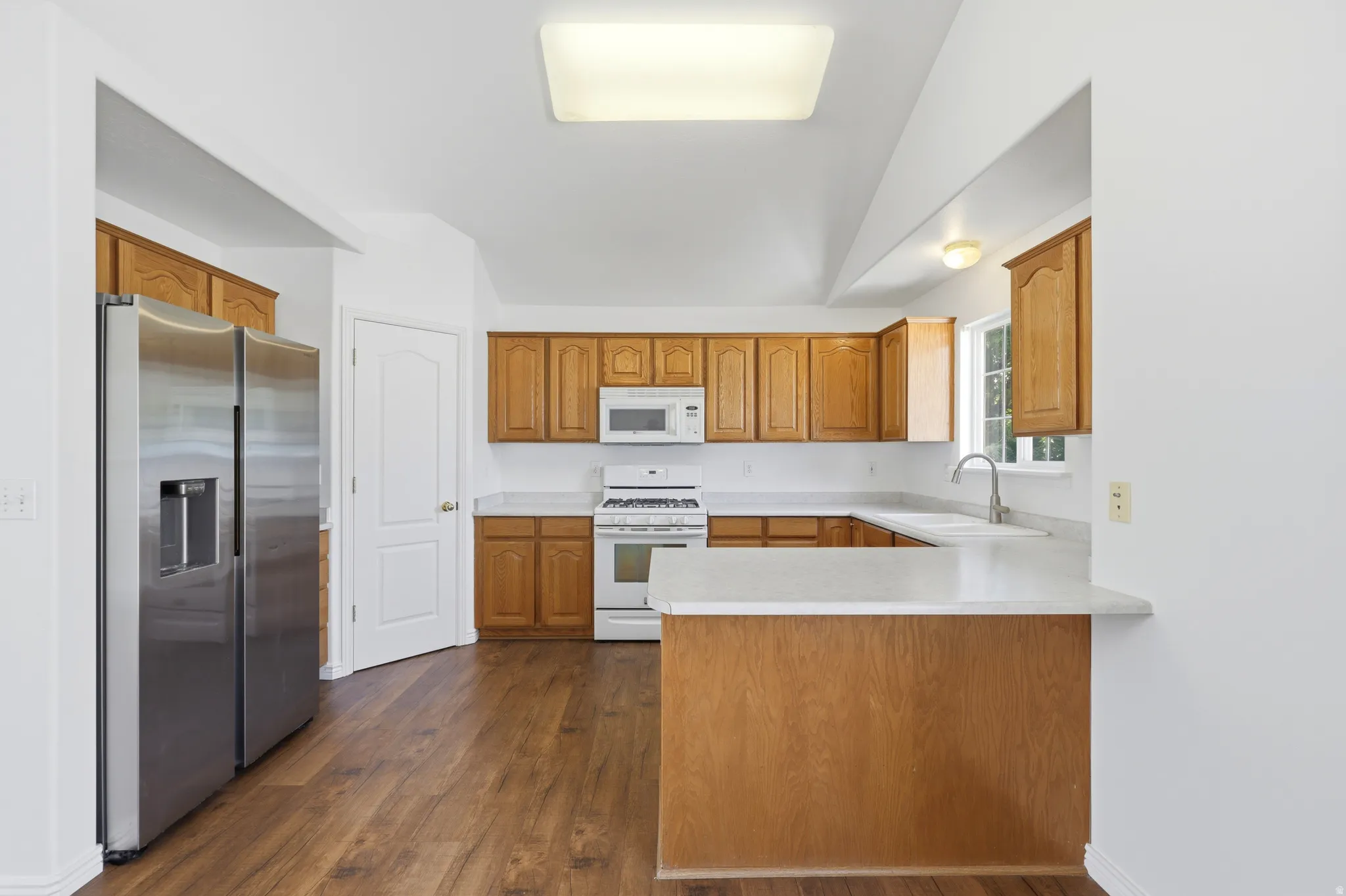 Kitchen featuring wood-finish flooring, wood cabinetry, white countertops, and a white gas range with an over-the-range microwave