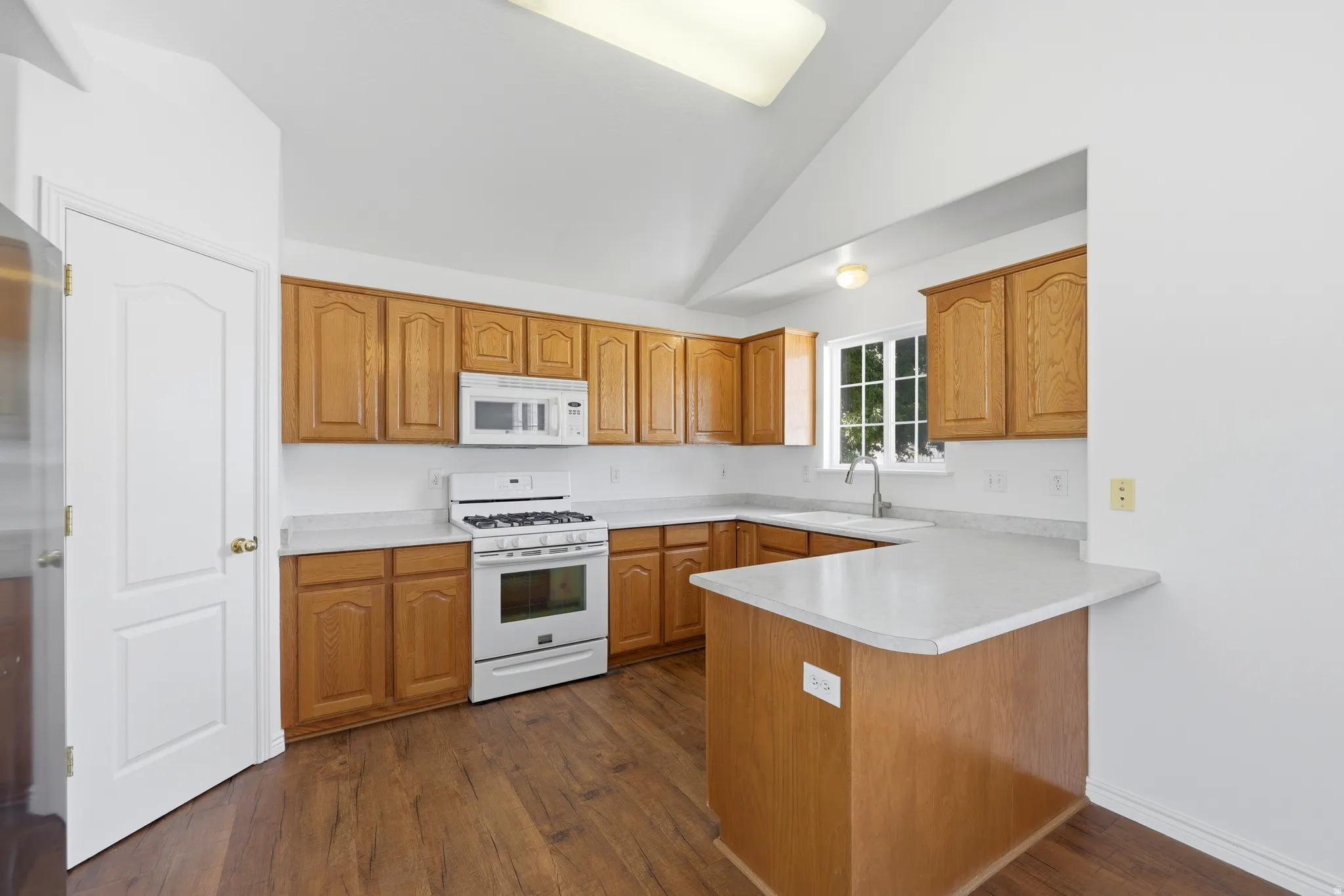 Kitchen featuring wood-finish flooring, light wood cabinetry, white countertops, and white appliances