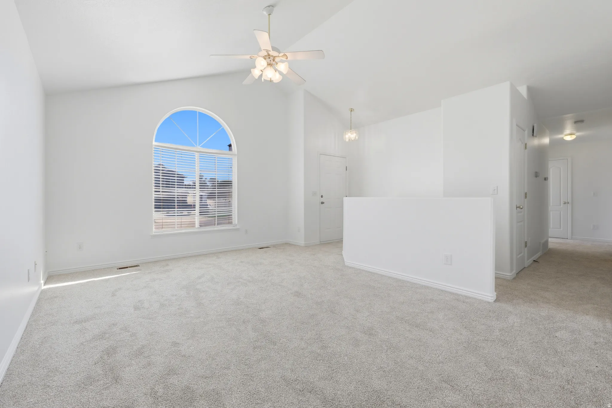 Bright interior room featuring a large arched window, vaulted ceiling, ceiling fan with light fixture, and light-toned carpeting