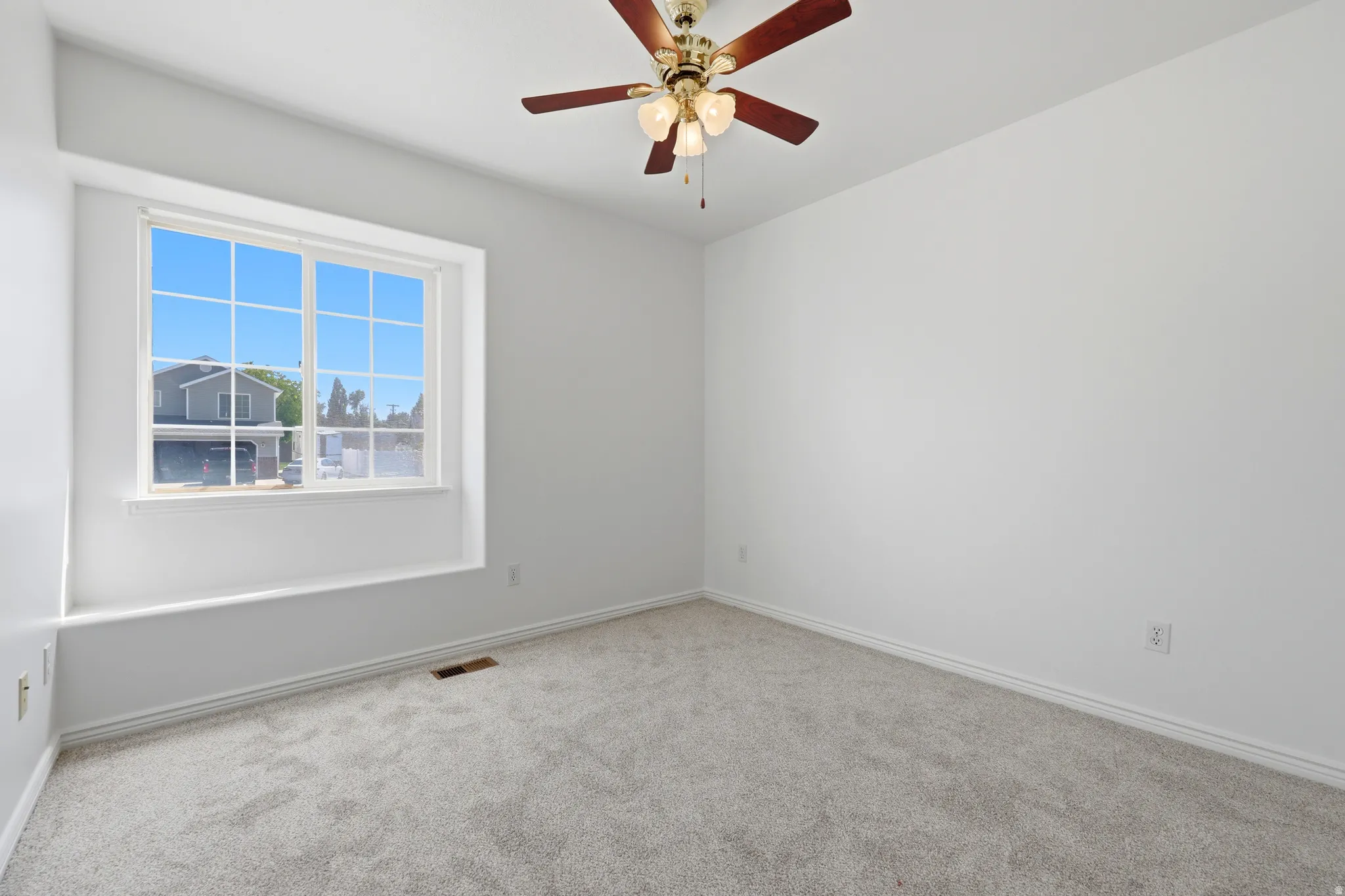 Bright room featuring a large window with white framing, light gray carpeting, and a ceiling fan with brass accents
