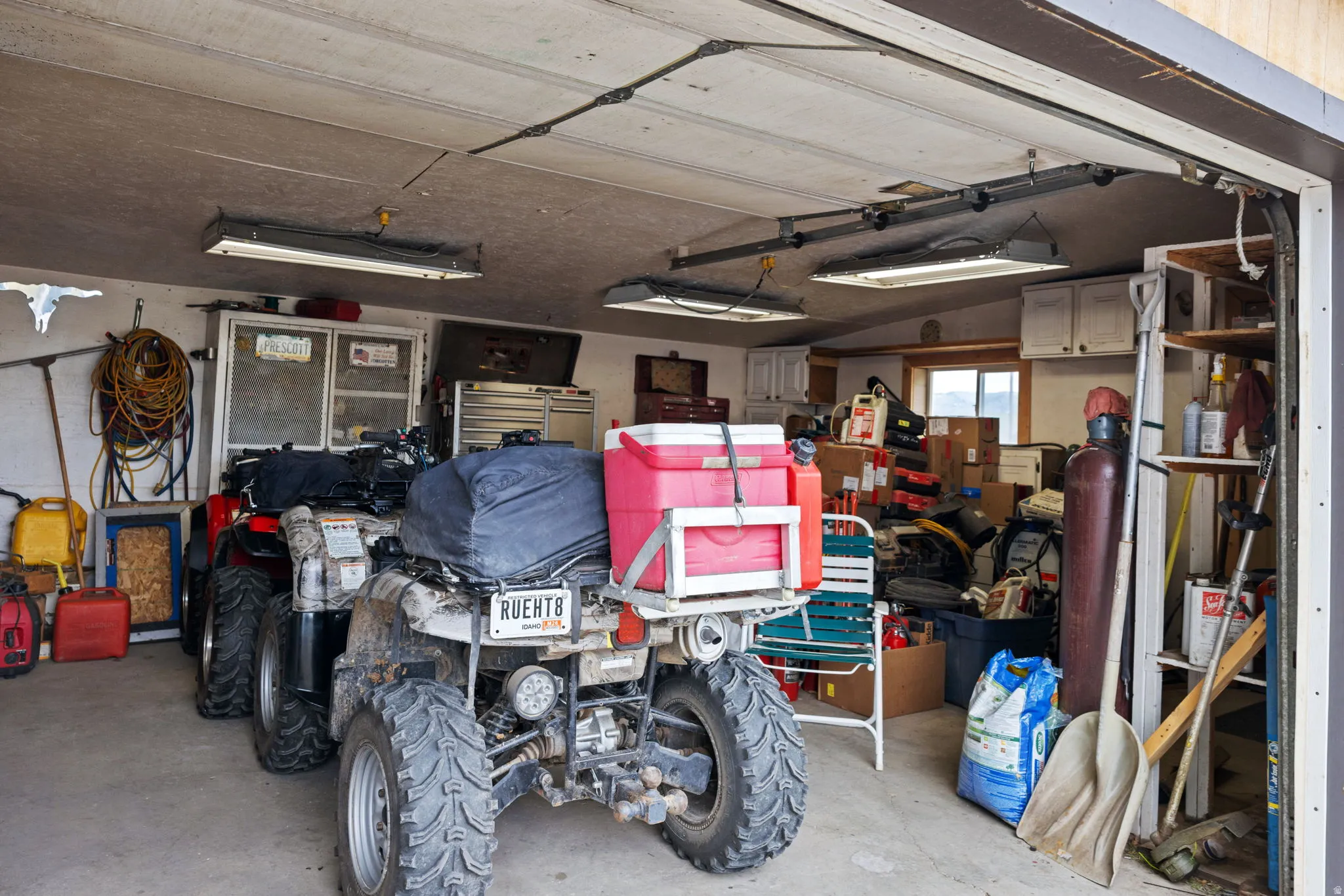 Spacious garage with concrete flooring, overhead fluorescent lighting, built-in shelving, and upper cabinetry