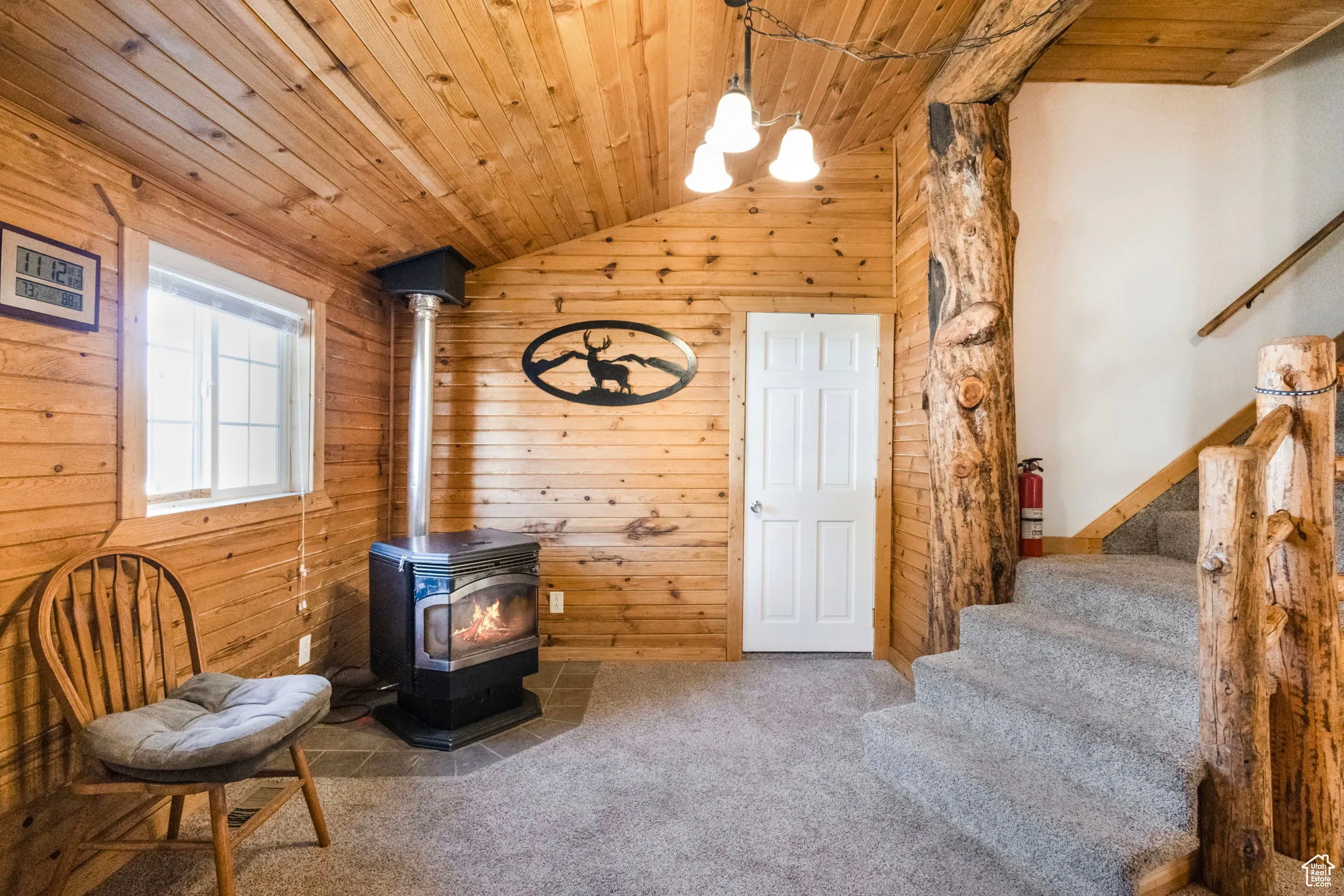 Living area featuring vaulted ceiling, stairway, a wood stove, wooden ceiling, and carpet