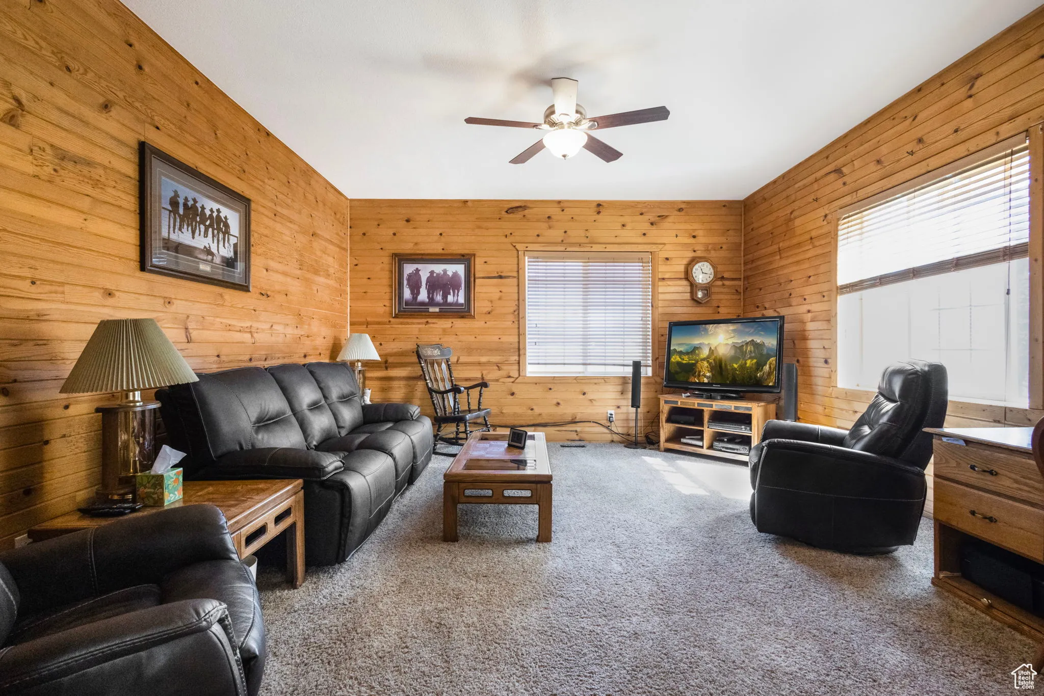 Living area featuring light carpet, wood walls, and a ceiling fan