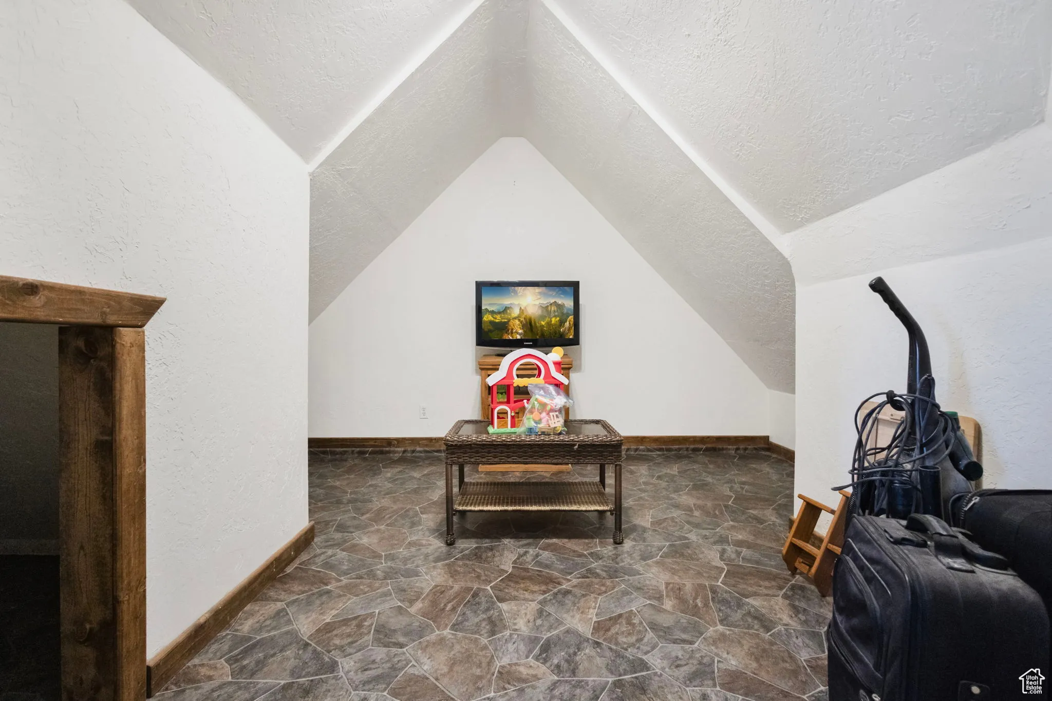 Additional living space featuring dark stone finish floors, a textured ceiling, and lofted ceiling