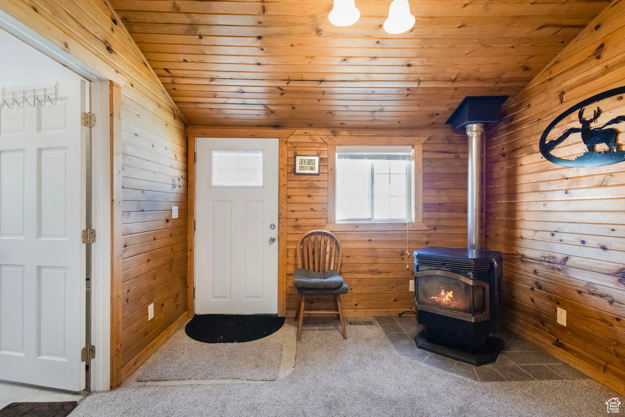 Foyer entrance with wood walls, vaulted ceiling, a wood stove, carpet, and wood ceiling