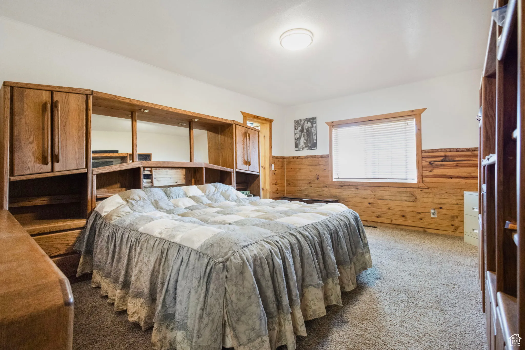 Carpeted bedroom featuring wooden walls, wainscoting, and a desk