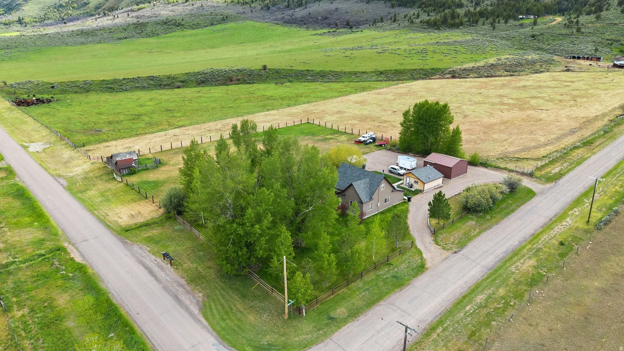 Expansive property featuring a residence with a dark shingle roof, surrounded by mature trees