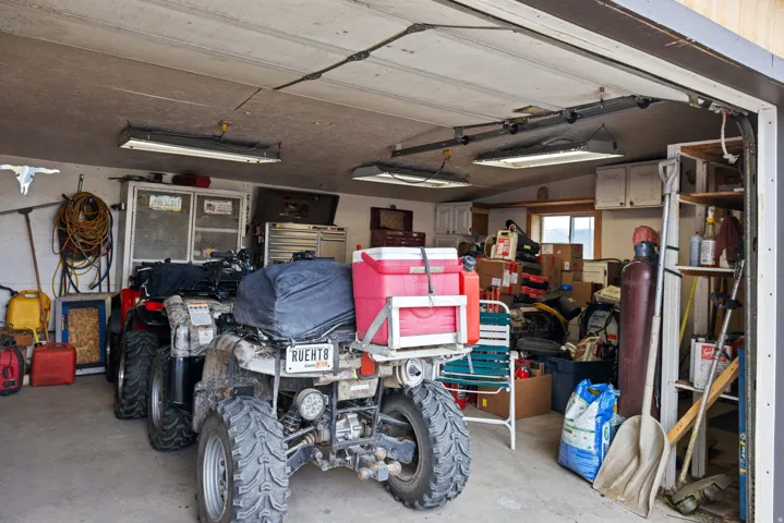 Spacious garage with concrete flooring, overhead fluorescent lighting, built-in shelving, and upper cabinetry