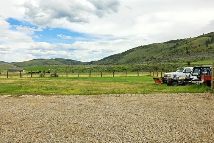 Expansive gravel parking area with a distant fenced pasture and rolling green hills