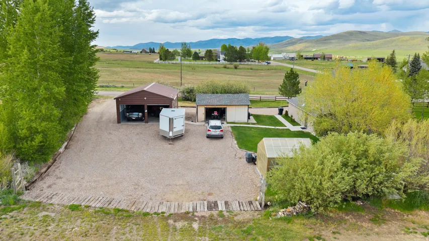 Expansive gravel driveway providing extensive parking and access to a detached multi-vehicle carport and a separate detached garage