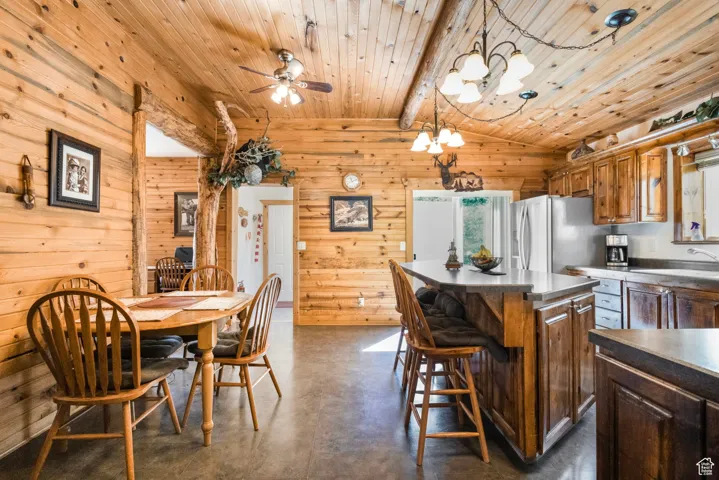 Dining room with finished concrete floors, wooden walls, ceiling fan, and a chandelier