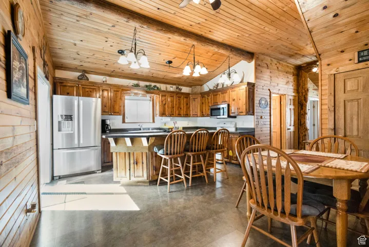 Kitchen featuring dark countertops, wood walls, appliances with stainless steel finishes, brown cabinets, and hanging light fixtures