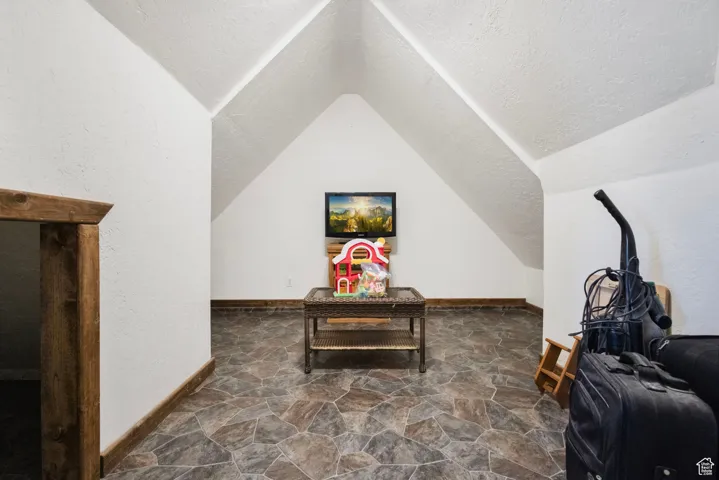 Additional living space featuring dark stone finish floors, a textured ceiling, and lofted ceiling