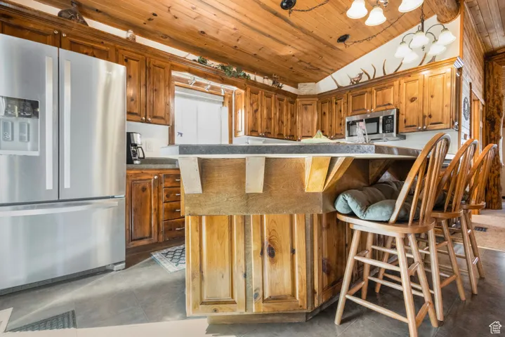 Kitchen featuring a breakfast bar, stainless steel appliances, lofted ceiling, wooden ceiling, and dark countertops