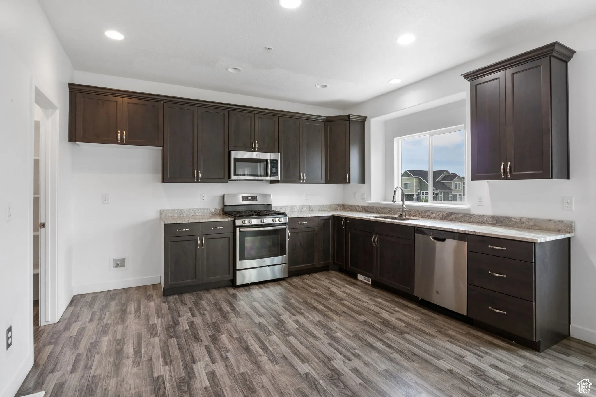 Kitchen featuring stainless steel appliances, dark brown cabinetry, dark wood-type flooring, and recessed lighting