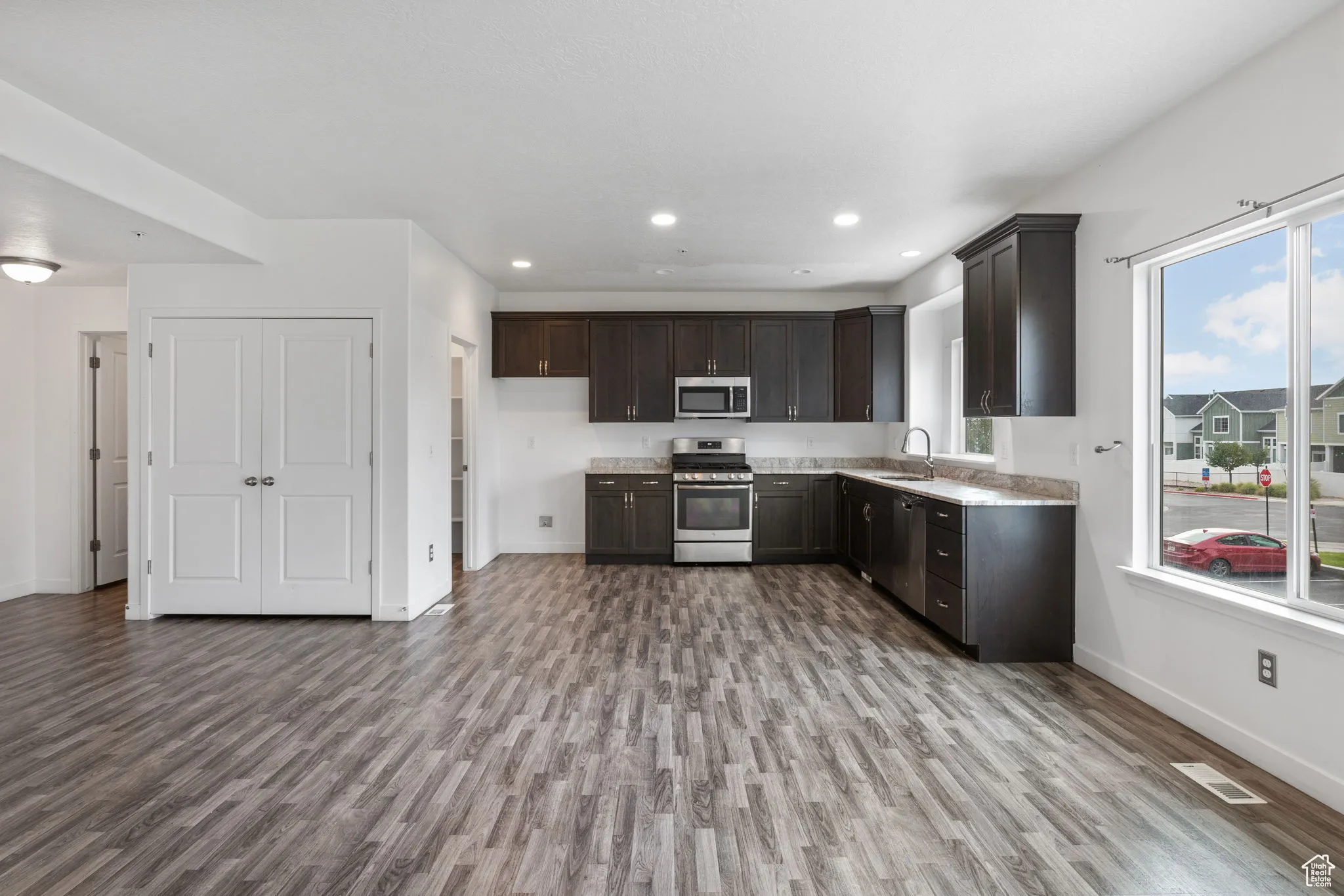 Kitchen with appliances with stainless steel finishes, dark brown cabinets, dark wood-style flooring, and recessed lighting