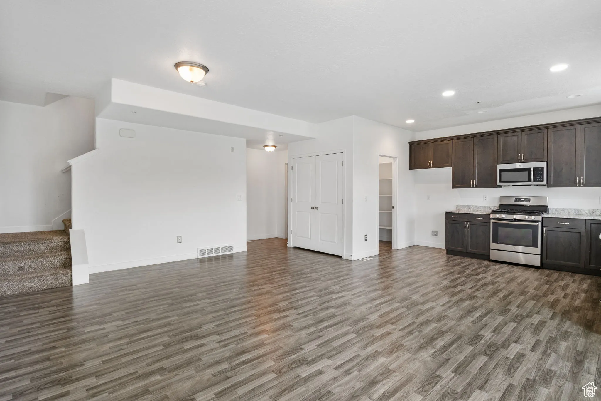 Kitchen with dark brown cabinets, appliances with stainless steel finishes, recessed lighting, dark wood-type flooring, and open floor plan