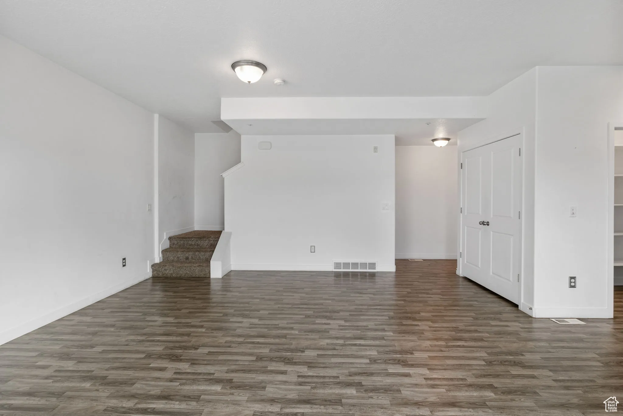 Unfurnished living room with stairs and dark wood-style flooring