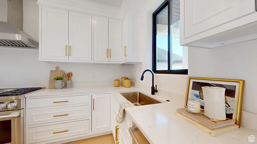 Kitchen with wall chimney range hood, stainless steel stove, white cabinetry, and light stone countertops