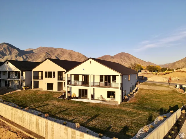 Back of property with a balcony, a patio, a mountain view, and a lawn