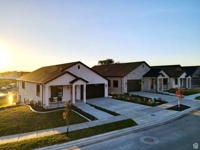 Modern farmhouse featuring concrete driveway, board and batten siding, a garage, stone siding, and a lawn