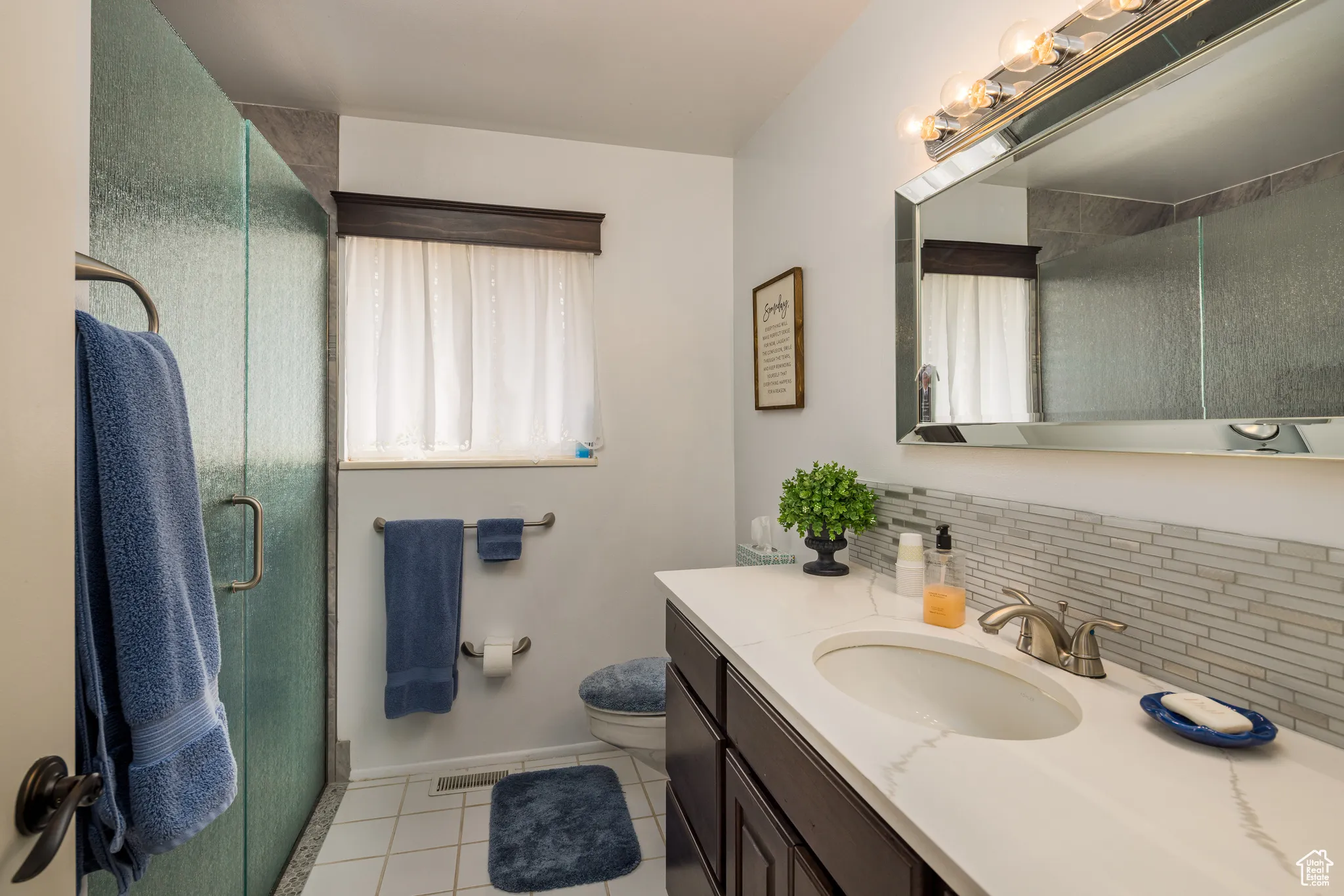 Bathroom with light tile patterned floors, backsplash, vanity, and a shower stall