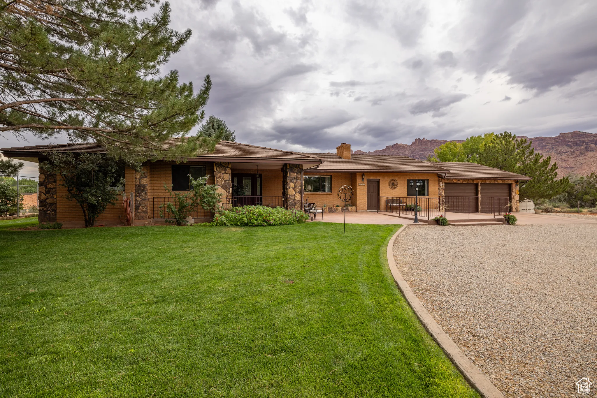 Ranch-style home featuring an attached garage, a front yard, concrete driveway, a chimney, and stone siding