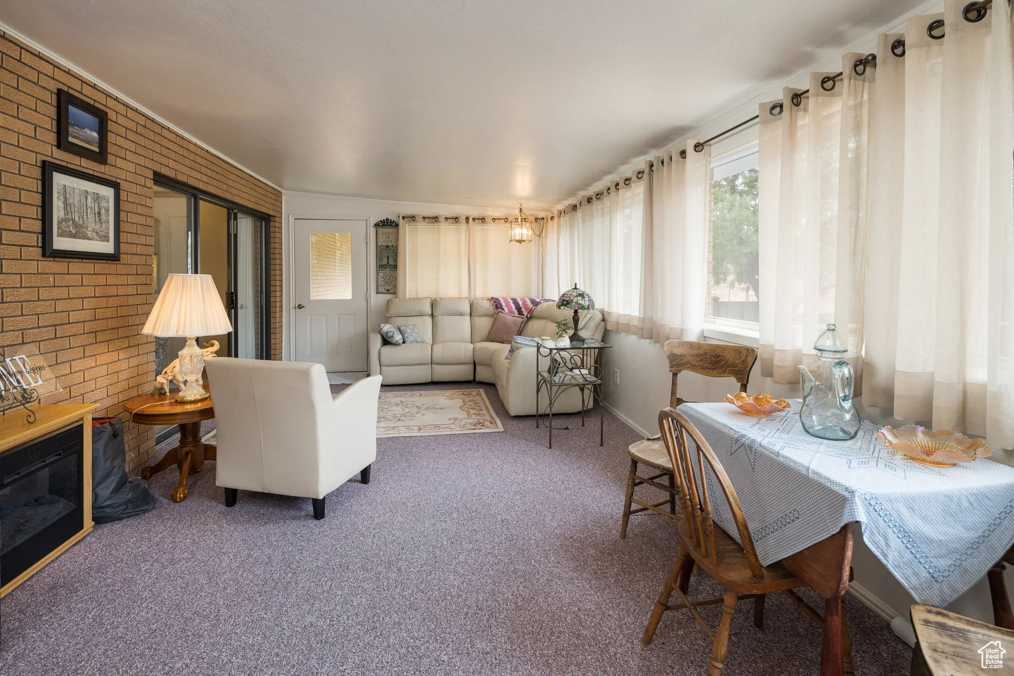 Living room featuring carpet, brick wall, and a chandelier