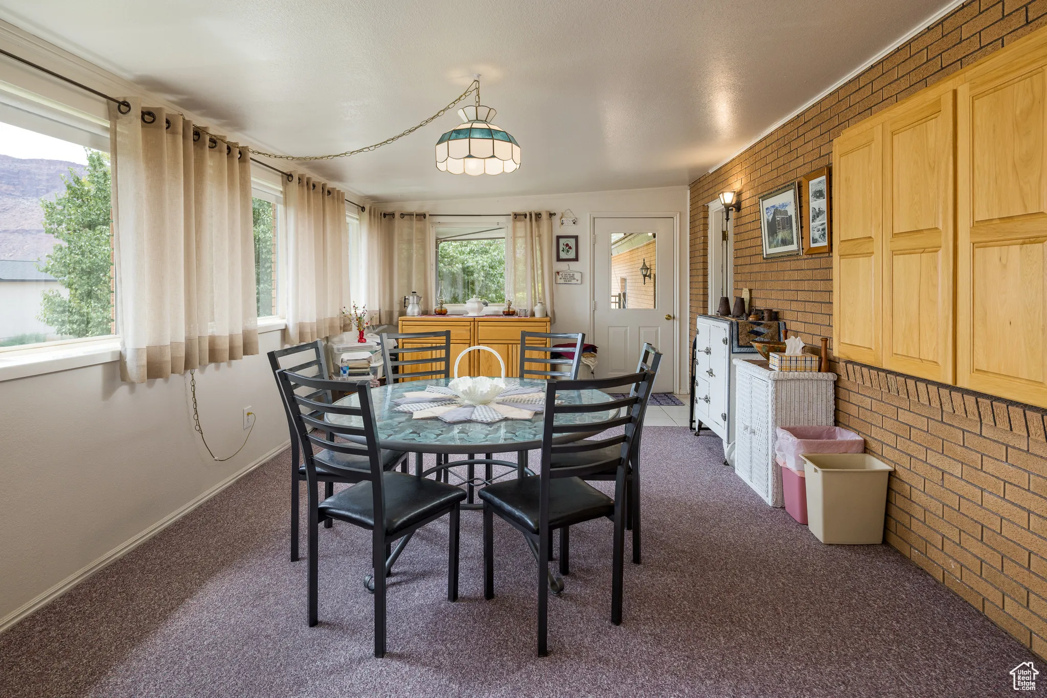 Carpeted dining space with brick wall and baseboards