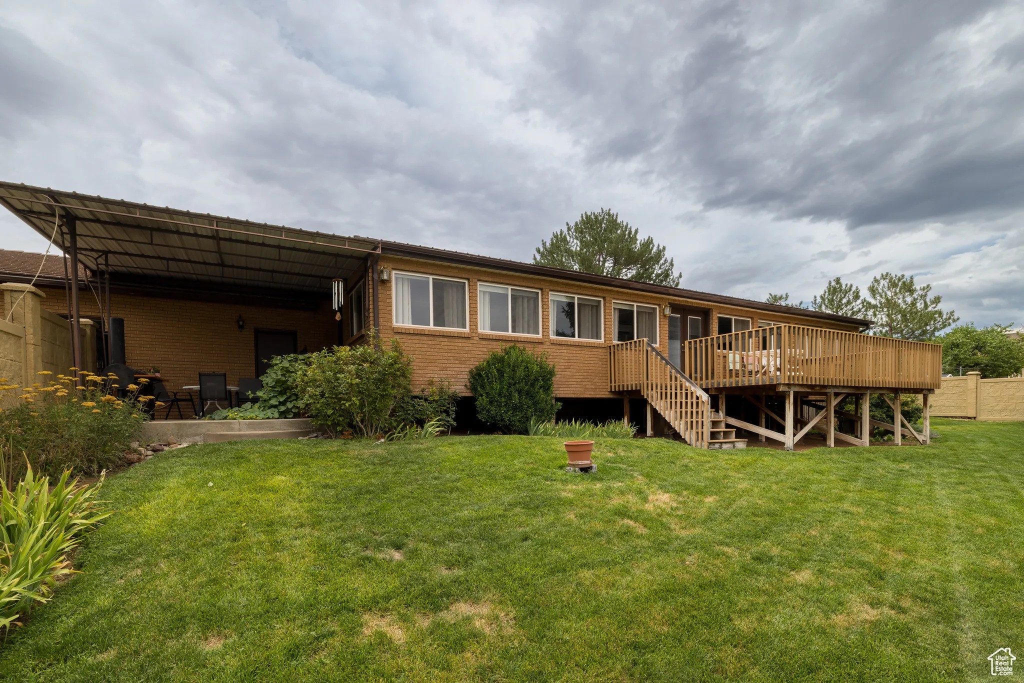Back of property featuring a lawn, brick siding, a wooden deck, and stairs