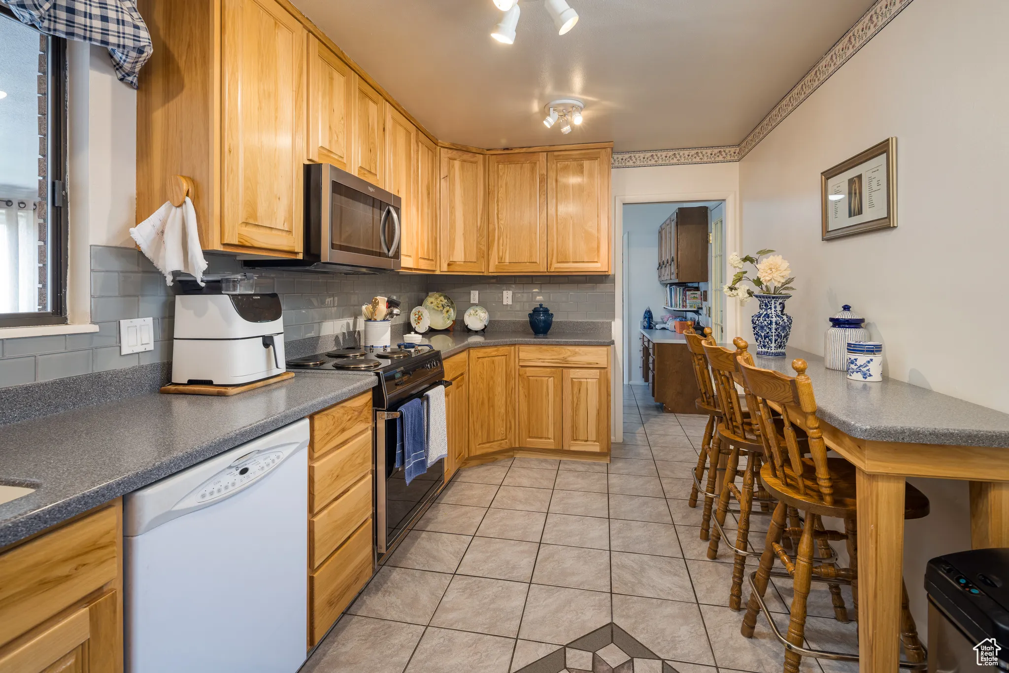 Kitchen featuring tasteful backsplash, light tile patterned floors, dishwasher, black gas range oven, and stainless steel microwave