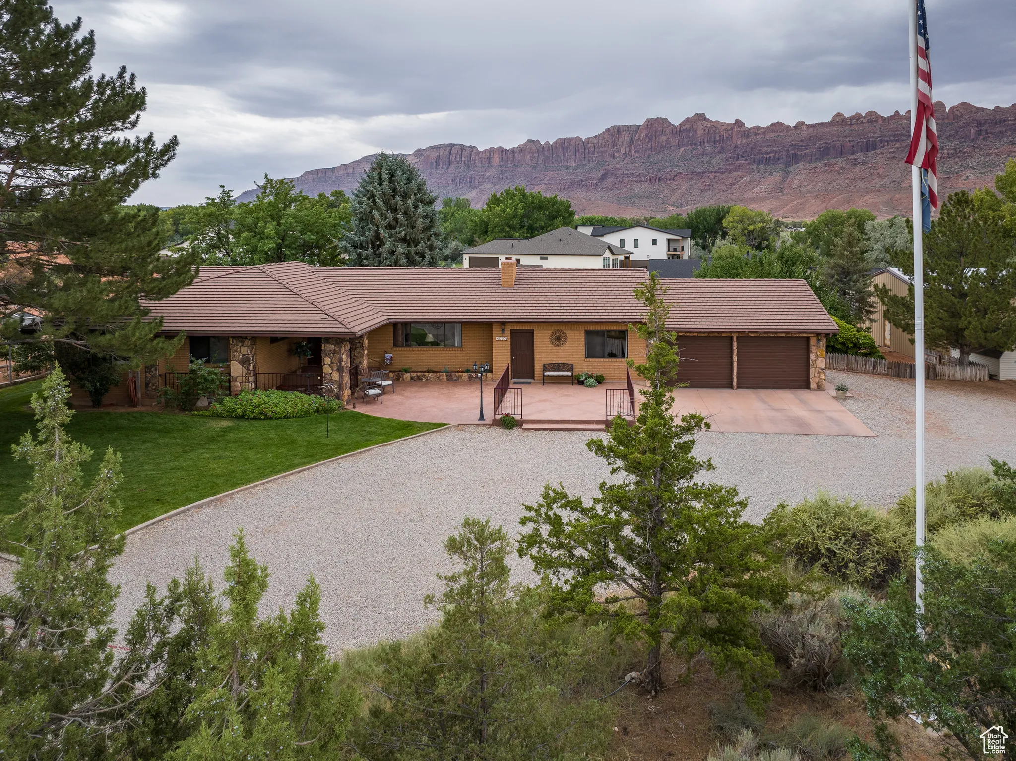 Ranch-style house featuring an attached garage, a tile roof, stone siding, a mountain view, and gravel driveway