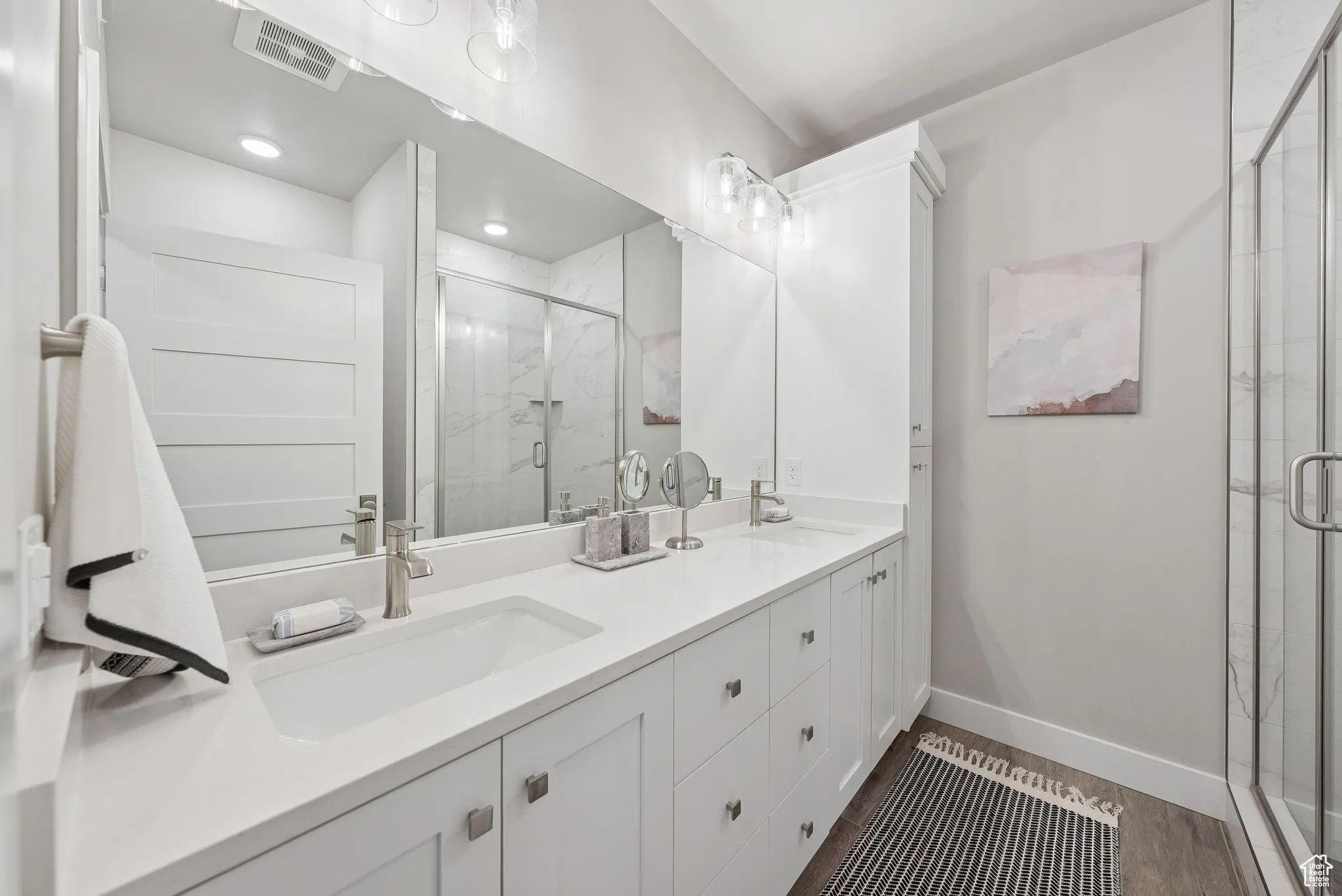 Full bath with double vanity, a marble finish shower, and dark wood-type flooring