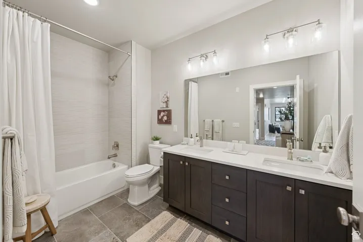 Full bathroom featuring shower / bathtub combination with curtain, double vanity, dark tile patterned floors, and recessed lighting