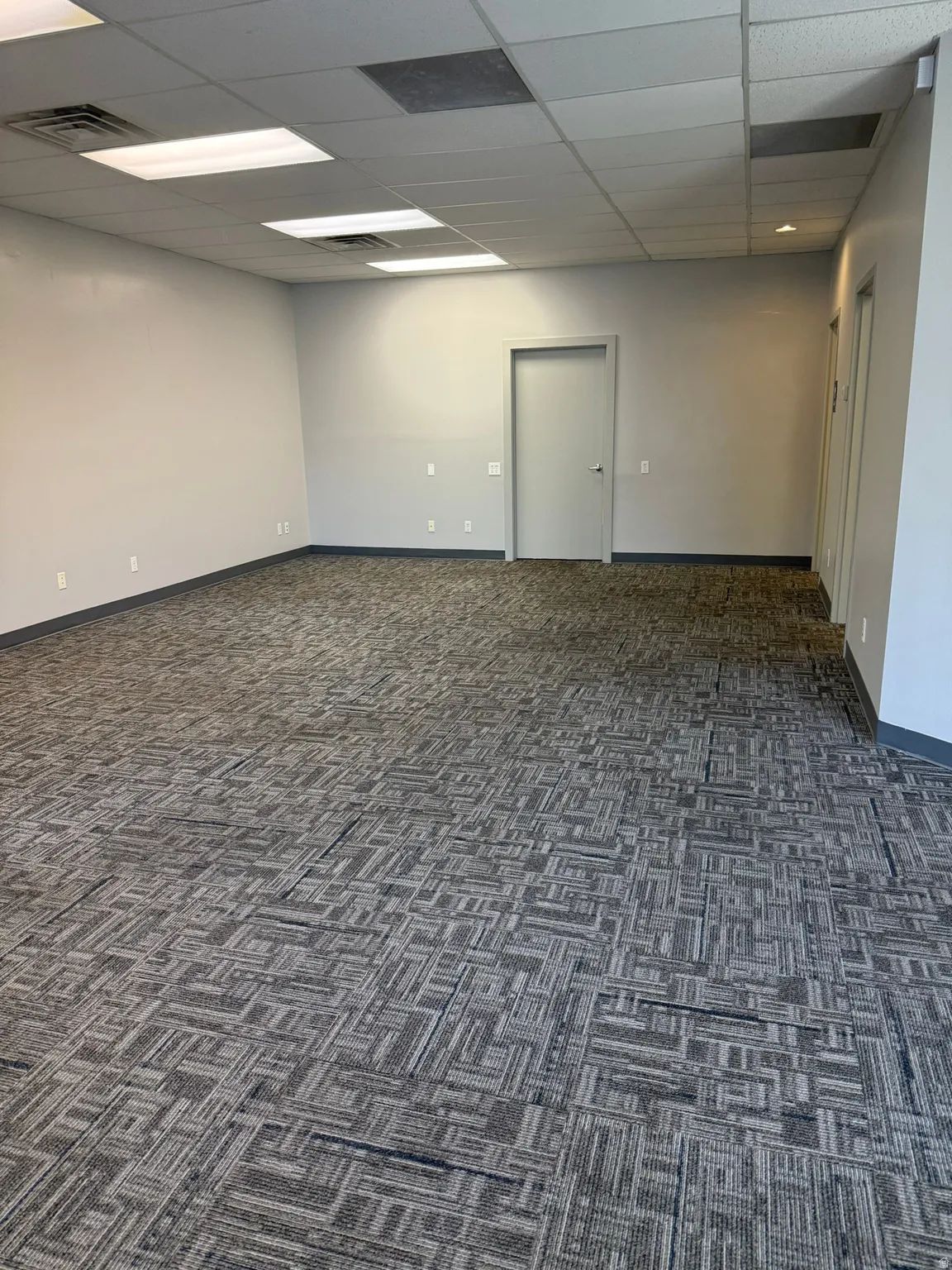 Empty room with a drop ceiling and dark colored carpet